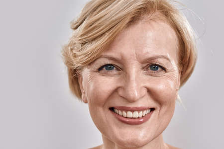 Close up shot of face of beautiful middle aged woman smiling at camera while posing isolated against...