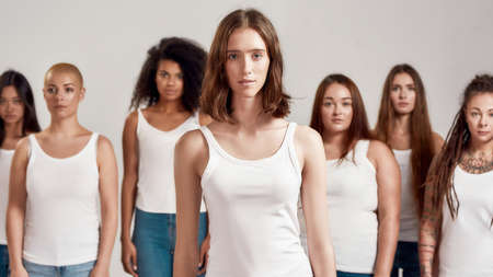 Portrait of young caucasian girl in white shirt looking at camera. Group of diverse women posing, standing isolated over grey backgroundの写真素材
