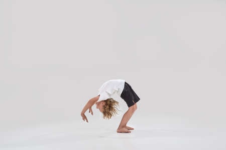 Full length shot of little playful boy child standing in bridge pose, bending over backwards isolated over grey backgroundの写真素材