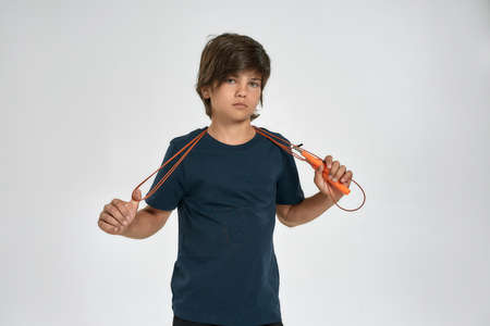 Little sportive boy child in sportswear looking at camera, holding jump rope while standing isolated...