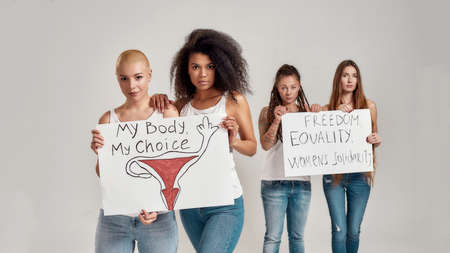 Four diverse women looking at camera while holding, standing with banners in their hands isolated over grey background. Feminism and equality conceptの写真素材