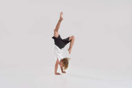 Full length shot of little playful boy child standing on his arms isolated over grey background