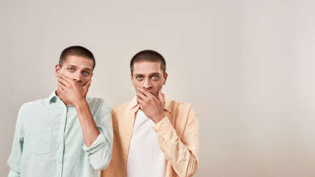 Two young scared twin brothers covering mouth with hand and looking at camera with shocked face...