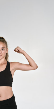 Cropped shot of cute sportive girl child in sportswear looking at camera, showing biceps while...