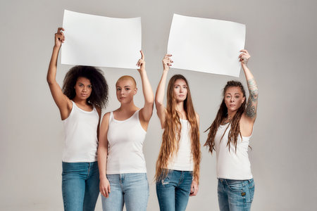 Four diverse women looking at camera while holding, standing with blank banners in their hands...