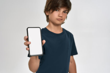 Little sportive boy child in sportswear holding, showing smartphone with blank screen, standing isolated over white backgroundの写真素材