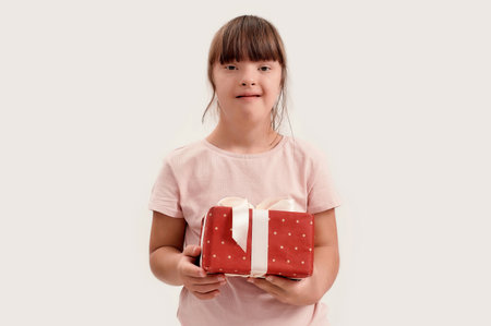 Portrait of disabled girl with Down syndrome smiling at camera, holding birthday present while posing isolated over white backgroundの写真素材