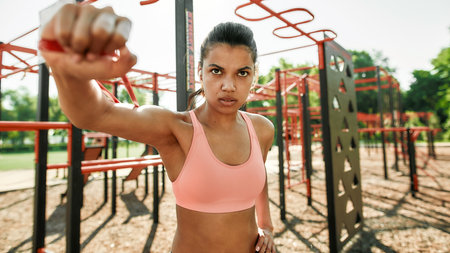 Portrait of concentrated young mixed race sportive woman having workout with rubber band at outdoor...