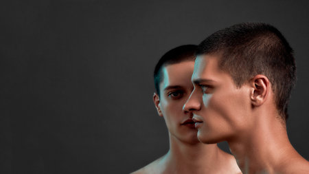 Front and side view of young twin brothers standing isolated over dark grey backgroundの写真素材