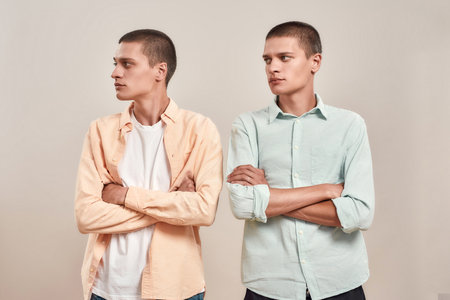 Two young caucasian men, twin brothers looking aside while posing together isolated over beige...
