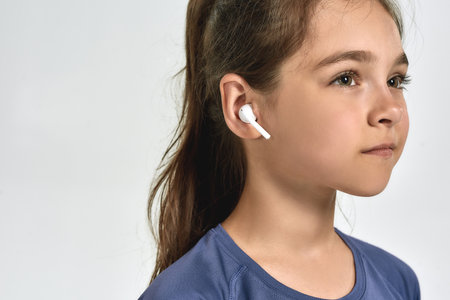 Close up portrait of little sportive girl child wearing earphones, listening to music, looking away...