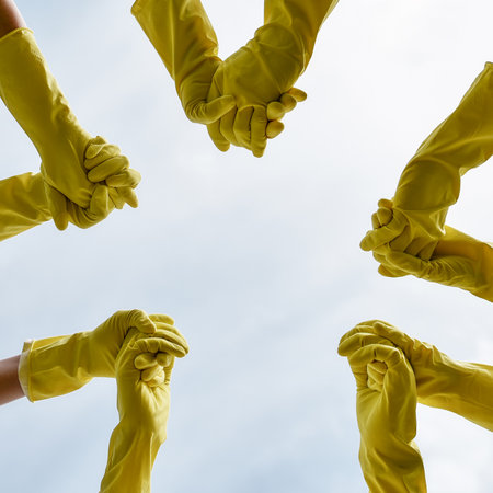 Group of eco activists or volunteers wearing yellow protective rubber gloves holding hands and...