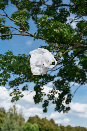 Save our planet. Vertical shot of a plastic bag hanging on a tree against blue skyの写真素材