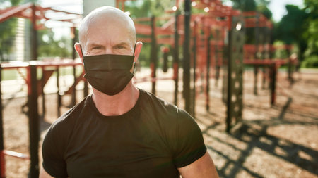 Close up portrait of sportive mature man wearing mask looking at camera, posing outdoors while exercising at street gym yardの写真素材