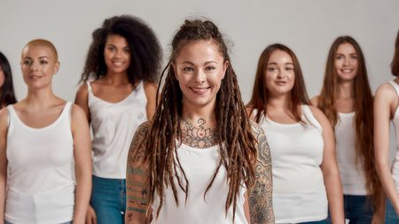 Close up portrait of young caucasian tattooed woman with dreadlocks in white shirt smiling at...