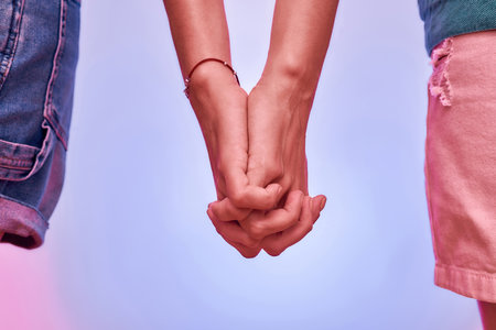 Close up of two girls, sisters holding hands together with fingers crossed isolated over purple background. Support, togetherness conceptの写真素材