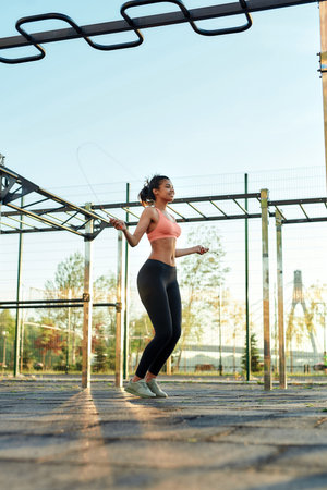 Young slim girl jumping with rope on sport ground