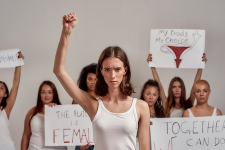 Beautiful young caucasian woman with short hair raised her fist, looking angry. Group of diverse...