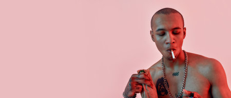 Dark-skinned tattooed topless guy smoking a cigarette, holding a lighter and bottle in paper bag