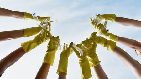Save our planet. Group of volunteers or eco activists wearing yellow protective rubber gloves holding plastic bottles against blue skyの写真素材