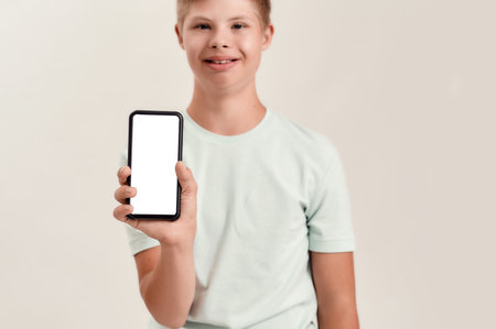 Close up of hand of disabled boy with Down syndrome holding smartphone with blank screen while standing isolated over white backgroundの写真素材