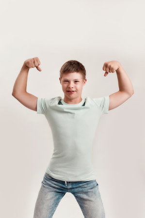 Cheerful disabled boy with Down syndrome looking at camera, raising his arms, showing his strength...