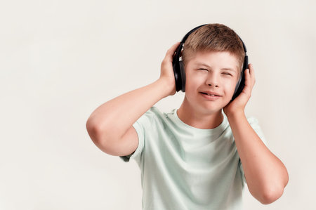 Portrait of happy disabled boy with Down syndrome in headphones listening to music while standing with eyes closed isolated over white backgroundの写真素材