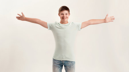 Happy disabled boy with Down syndrome smiling at camera while posing, standing with arms wide open, outstretched isolated over white backgroundの写真素材