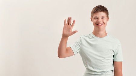 Happy disabled boy with Down syndrome smiling and waving at camera while posing isolated over white backgroundの写真素材