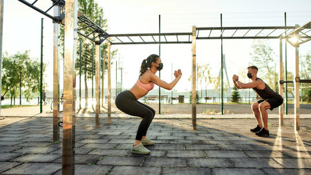 Couple of athletes doing squats on urban sport ground