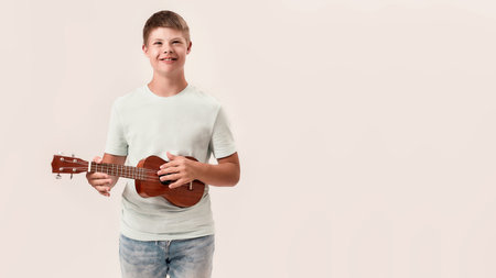Cheerful disabled boy with Down syndrome smiling while playing ukulele, standing isolated over white backgroundの写真素材
