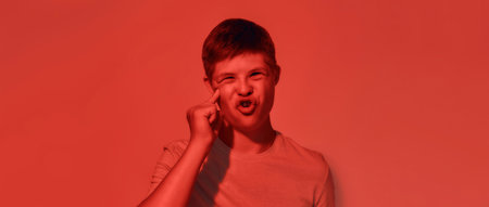 Portrait of teenaged disabled boy with Down syndrome looking emotional while posing isolated over red light backgroundの写真素材