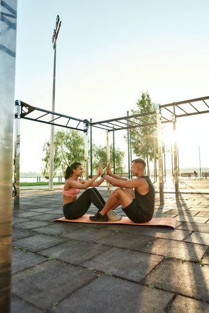Young mixed race sportsmen pair clapping hands while training together on urban sport playground