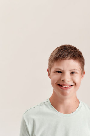 Close up portrait of cheerful disabled boy with Down syndrome smiling at camera while posing isolated over white backgroundの写真素材