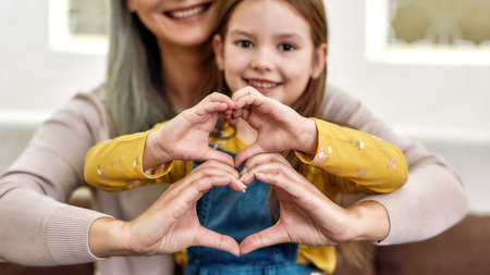 Spreading love. Close up portrait of little girl granddaughter spending time together with her loving granny. They are smiling and showing heart signの写真素材