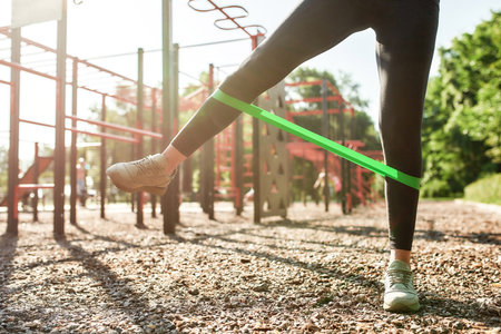 Close up of legs of young woman training with elastic band at ou