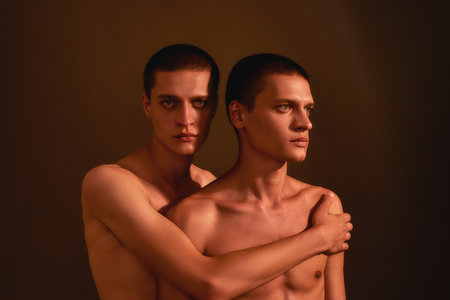 Portrait of young half naked twin brothers posing together in studio, standing isolated over brown background, front viewの写真素材