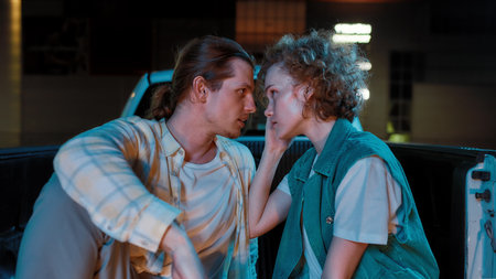 A close up of two young fashionably dressed white friends of different genders looking at each other...