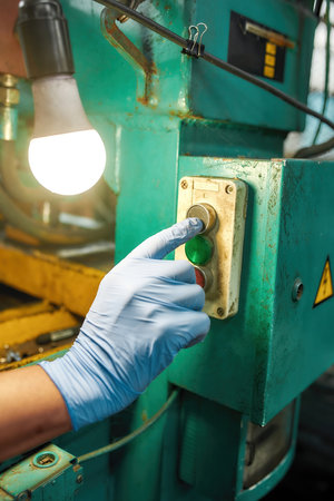 Hand in glove pushing button on industrial pressの写真素材