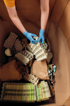 Hands in gloves putting egg trays into large box