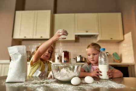Two little kids, boy and girl adding flour, milk and other ingredients while cooking, preparing...