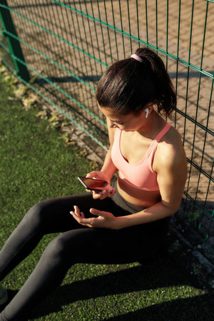 Young sportive girl wearing earphones relaxing on the field outd