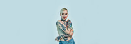 Tattoo and piercing. A white tattoed pierced woman standing topless with her hands crossed on her chest covering her breastsの写真素材