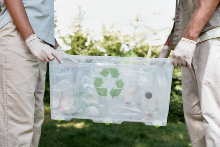 Cropped shot of two volunteers holding recycle bin with plastic waste while standing in the forest or parkの写真素材