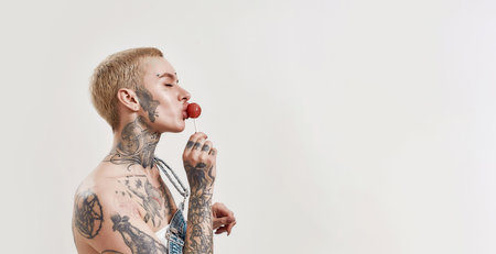Multicultural relationship. A white pierced woman with a lollipop and a dark-skinned man both tattooed standing next to each otherの写真素材