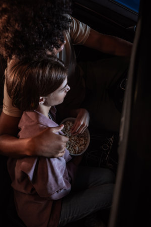 Top view of a young couple embracing each other, watching a movie, having popcorn while sitting together in the car parked in front of a big screen in an open air cinemaの写真素材