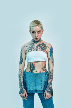 Tattoo and piercing. A white woman with piercing and tattoos standing in front of a camera looking into it wearing a denim overallの写真素材