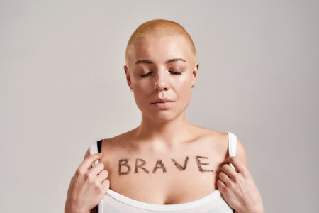 Portrait of a beautiful young caucasian woman showing her chest with the word Brave painted on it while posing with eyes closed isolated over grey backgroundの写真素材