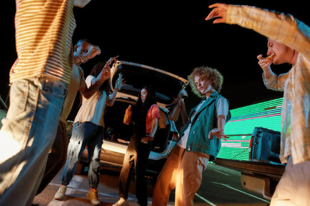A close up of a good-looking group of youngsters of different nationalities dancing in front of each other outside on a parking site while eating pizza and drinking beerの写真素材