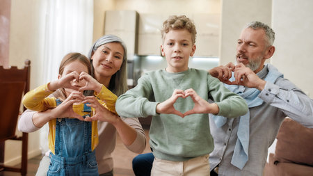Happy caucasian family, grandparents and grandchildren making heart sign with hands and smiling at camera while sitting on the floor at homeの写真素材